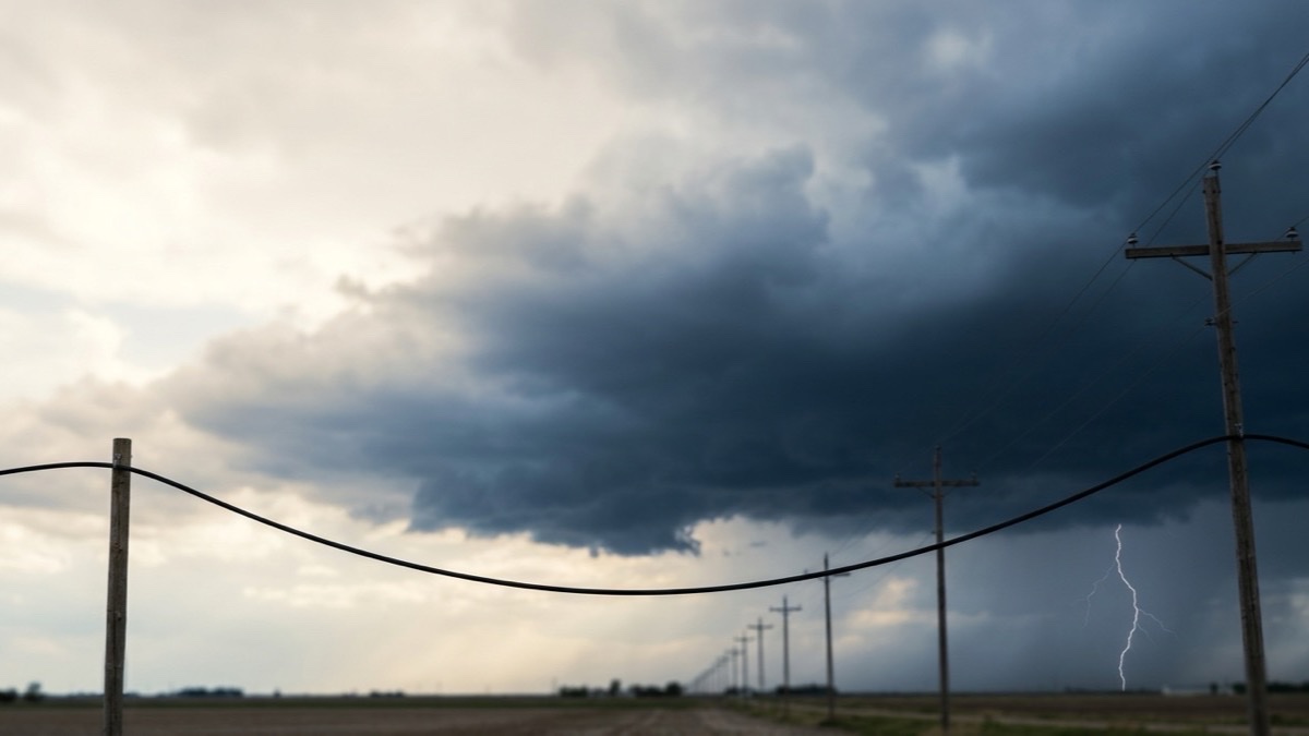 Black all-dielectric fiber optic cable strung on rural poles beneath a storm sky with distant lightning